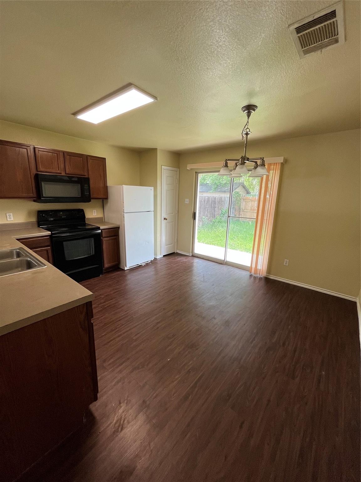 3001 Caleb Drive Austin, TX 78725 - Photo 5 of 16 Kitchen with black appliances, light countertops, dark wood-style floors, a textured ceiling, and pendant lighting