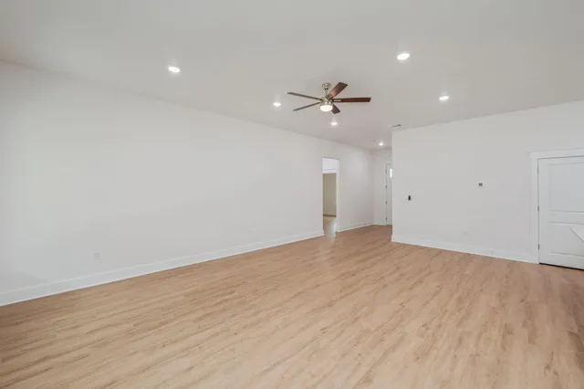 a view of an empty room with wooden floor and a ceiling fan