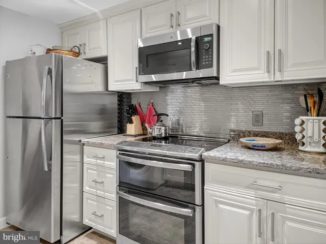 a kitchen with stainless steel appliances granite countertop white cabinets a refrigerator and a stove top oven