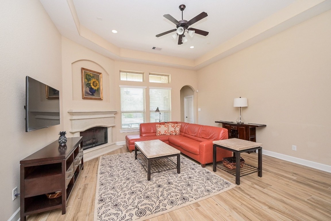 107 North Bacopa Drive Spring, TX 77389 - Photo 7 of 34 Spacious living room with high tray ceilings, recessed lighting, and a ceiling fan, centered around a cozy fireplace and framed by tall windows.