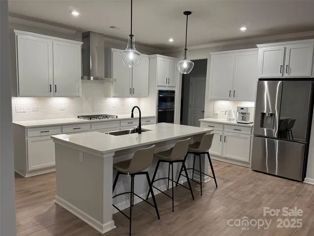 a kitchen with stainless steel appliances granite countertop a sink a stove a refrigerator and island with wooden floor