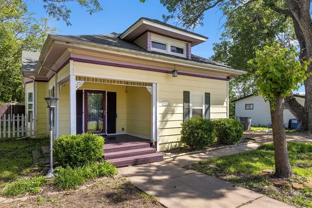 a view of a house with brick walls plants and large tree