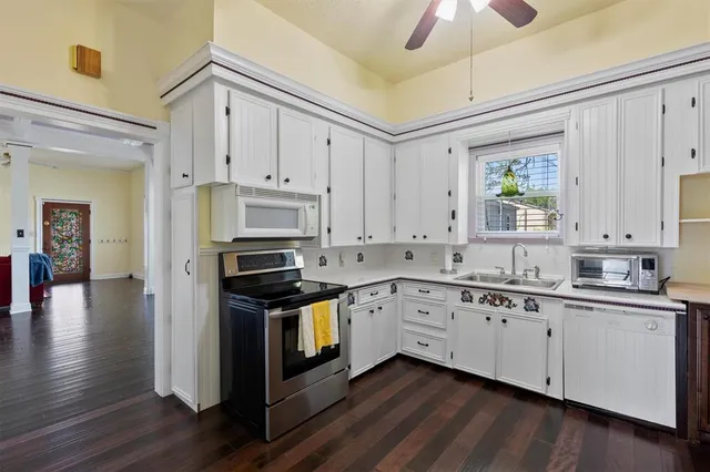 a kitchen with granite countertop a stove a sink and white cabinets with wooden floor next to windows