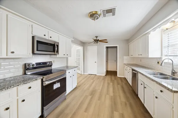 a kitchen with granite countertop a stove top oven a sink dishwasher a dining table and chairs with wooden floor