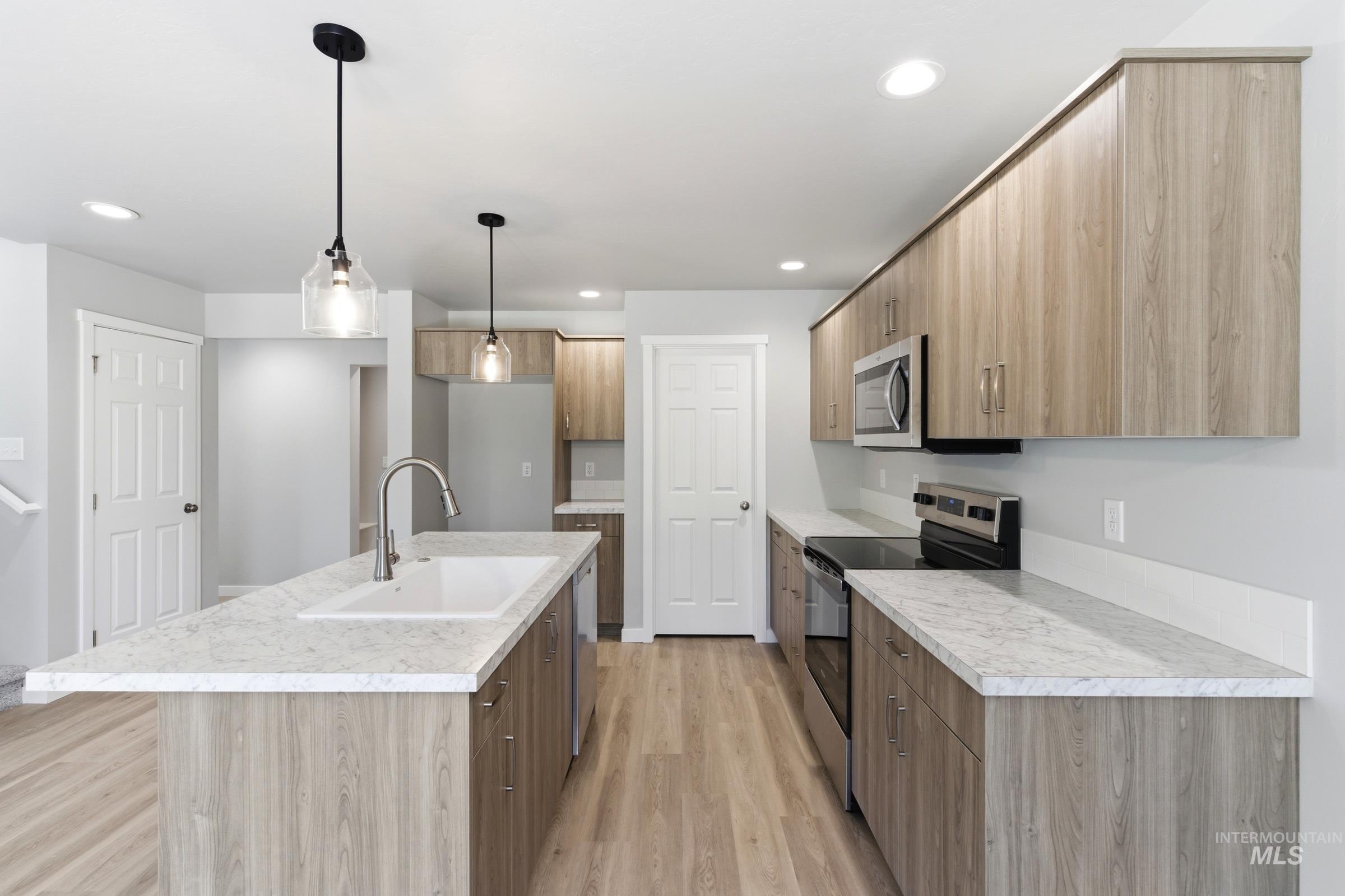 2374 West Fallon Loop Nampa, ID 83651 - Photo 6 of 24 Modern kitchen featuring a spacious island with an integrated sink, wood-finish cabinetry, stainless steel appliances, recessed lighting, and pendant fixtures