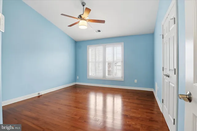 an empty room with wooden floor chandelier fan and windows