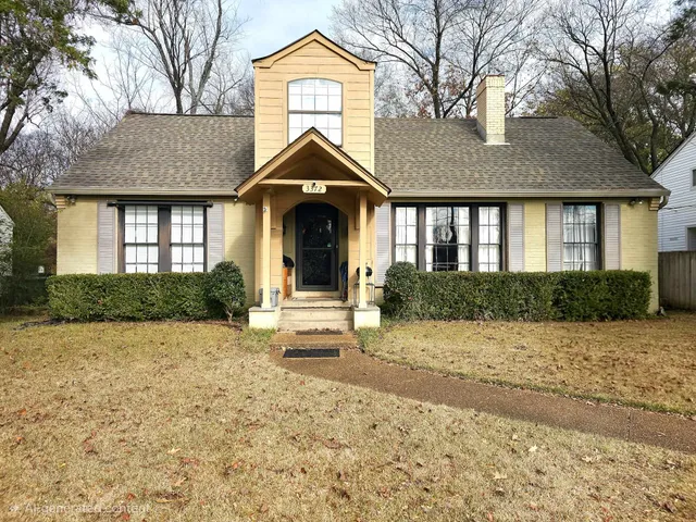 a view of a brick house with plants and large trees