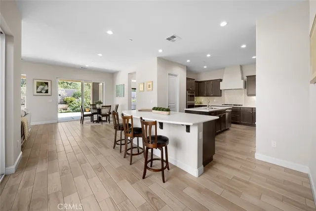 a open kitchen with stainless steel appliances granite countertop a stove top oven a sink a dining table and chairs with wooden floor