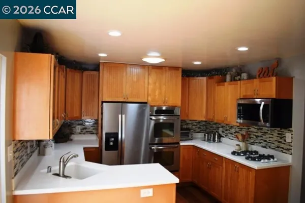 a kitchen with stainless steel appliances granite countertop a refrigerator a stove and a sink with wooden cabinets