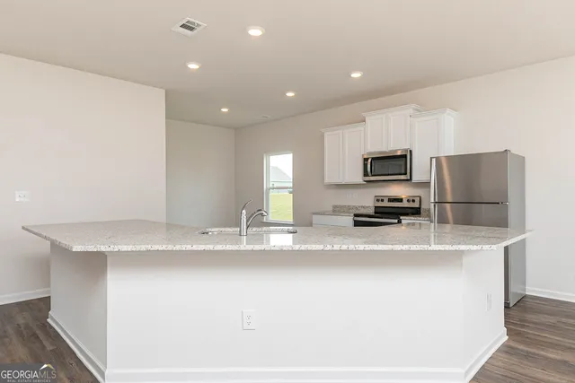 a kitchen with stainless steel appliances granite countertop a sink a stove a refrigerator a sink with white cabinets and wooden floor