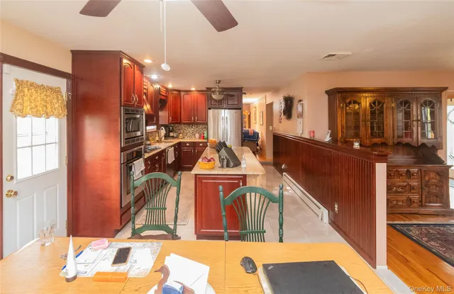 a living room with stainless steel appliances kitchen island granite countertop a table chairs and a refrigerator