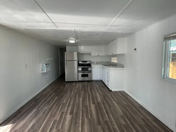 a big room with wooden floor electronic appliances and windows