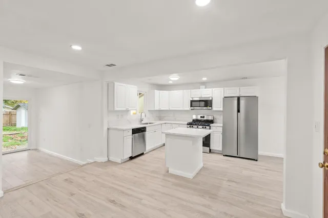 a large white kitchen with stainless steel appliances granite countertop a stove a sink dishwasher and a refrigerator with wooden floor