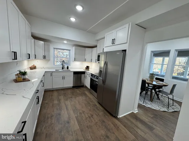 a kitchen with granite countertop a refrigerator oven a sink dishwasher and white cabinets with wooden floor