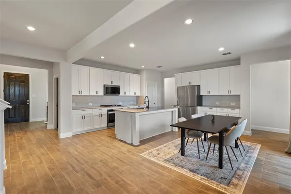 a large white kitchen with stainless steel appliances kitchen island granite countertop a refrigerator a stove a sink a dining table and chairs with wooden floor