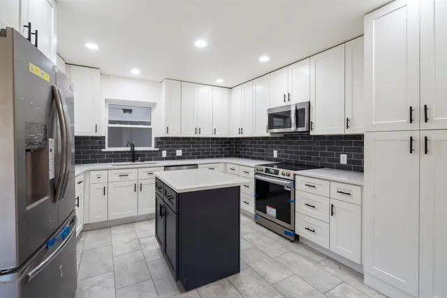 a kitchen with stainless steel appliances granite countertop a stove top oven a refrigerator a sink and white cabinets