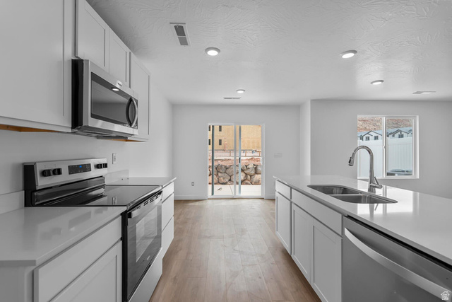 2133 Wolverine Way, Unit 2440 Washington, UT 84780 - Photo 9 of 39 Modern kitchen featuring white cabinetry, stainless steel appliances, wood-finish flooring, recessed lighting, and a kitchen island with an integrated sink
