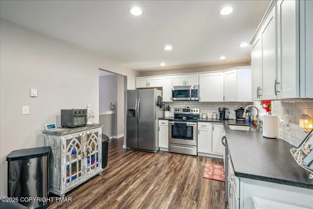 a kitchen with stainless steel appliances granite countertop a refrigerator oven a sink dishwasher and white cabinets with wooden floor