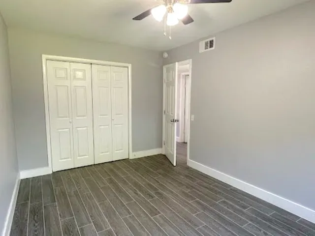 an empty room with wooden floor closet and windows