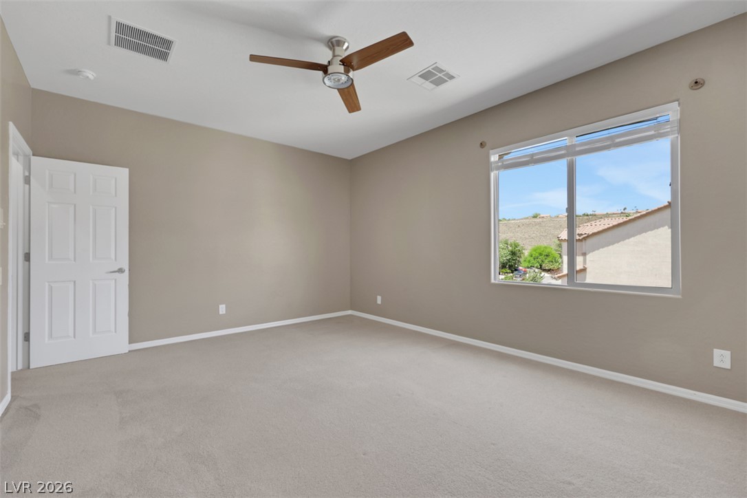2501 Bechamel Place Henderson, NV 89044 - Photo 34 of 50 An airy primary bedroom provides ample space and natural light, featuring plush carpeting and a modern ceiling fan.