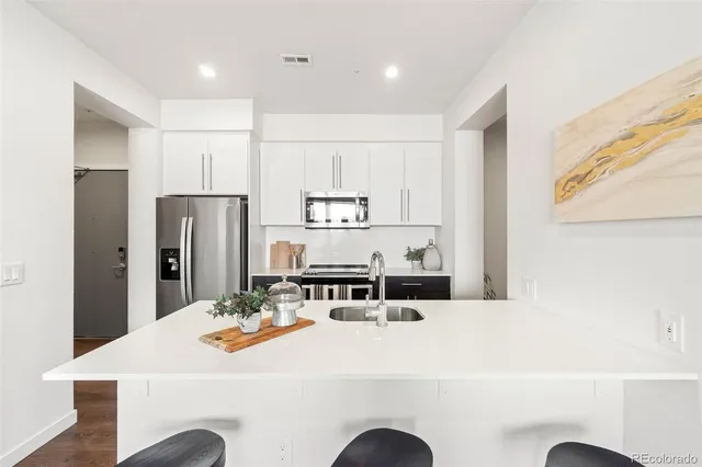 a kitchen with stainless steel appliances kitchen island granite countertop a refrigerator a stove a sink and white cabinets with wooden floor