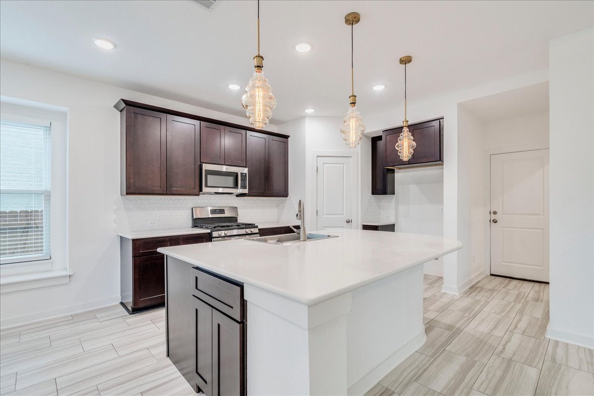 8008 Prairie Rye Drive Lago Vista, TX 78645 - Photo 4 of 40 Kitchen featuring a large island with a white countertop, dark wood-finish cabinetry, stainless steel appliances, and wood-finish flooring