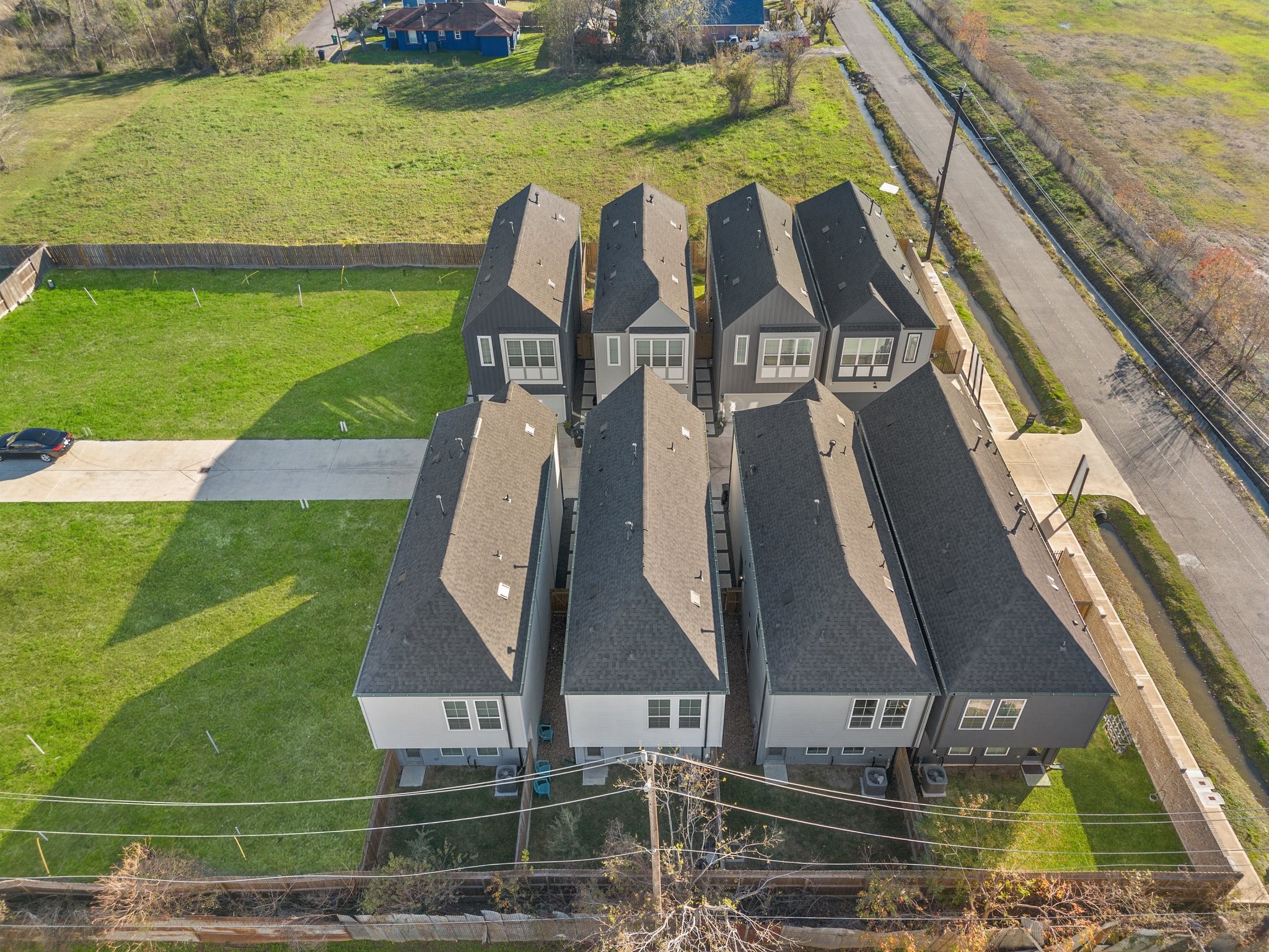 2928 Stevens Street Houston, TX 77026 - Photo 26 of 30 This aerial photo shows a row of modern townhomes with dark roofs and light siding. They are situated in a quiet, green neighborhood, with a paved road and ample surrounding lawn space. The area appears to be well-maintained and offers a peaceful setting.
