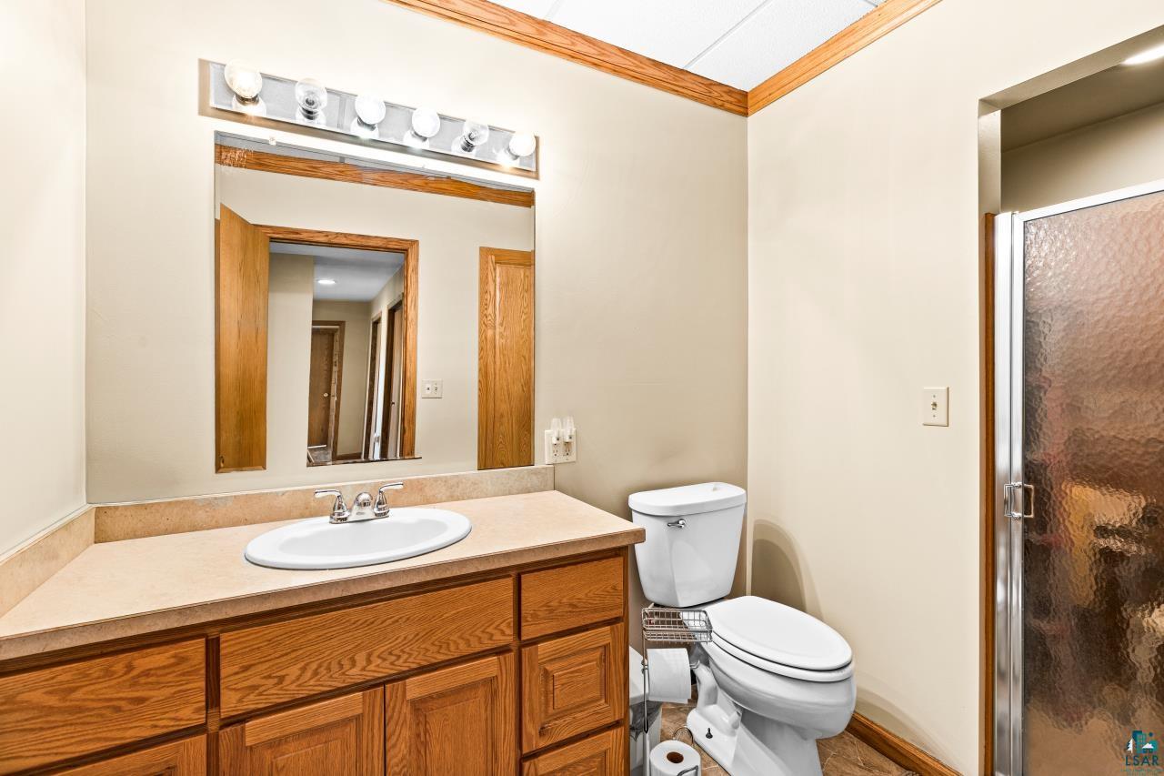 4800 Tower Road Moose Lake, MN 55767 - Photo 62 of 83 Bathroom featuring a wood-finish vanity with an integrated sink, a neutral-toned countertop, a large wall-mounted mirror, and a glass-enclosed shower with a textured panel