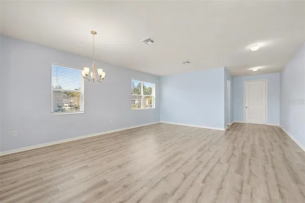 an empty room with wooden floor chandelier and windows