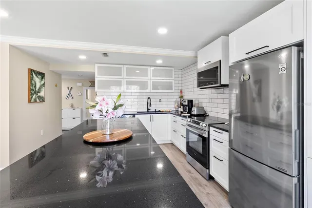 a kitchen with stainless steel appliances granite countertop a refrigerator a stove a sink a dining table and chairs with wooden floor