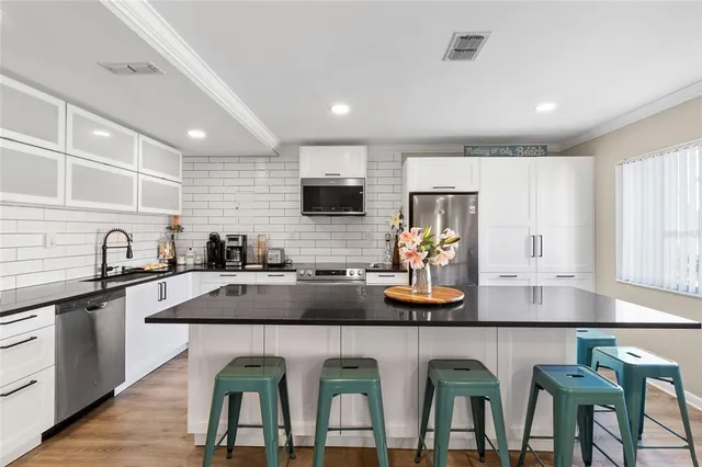 a kitchen with white cabinets a sink stove and refrigerator with wooden floor