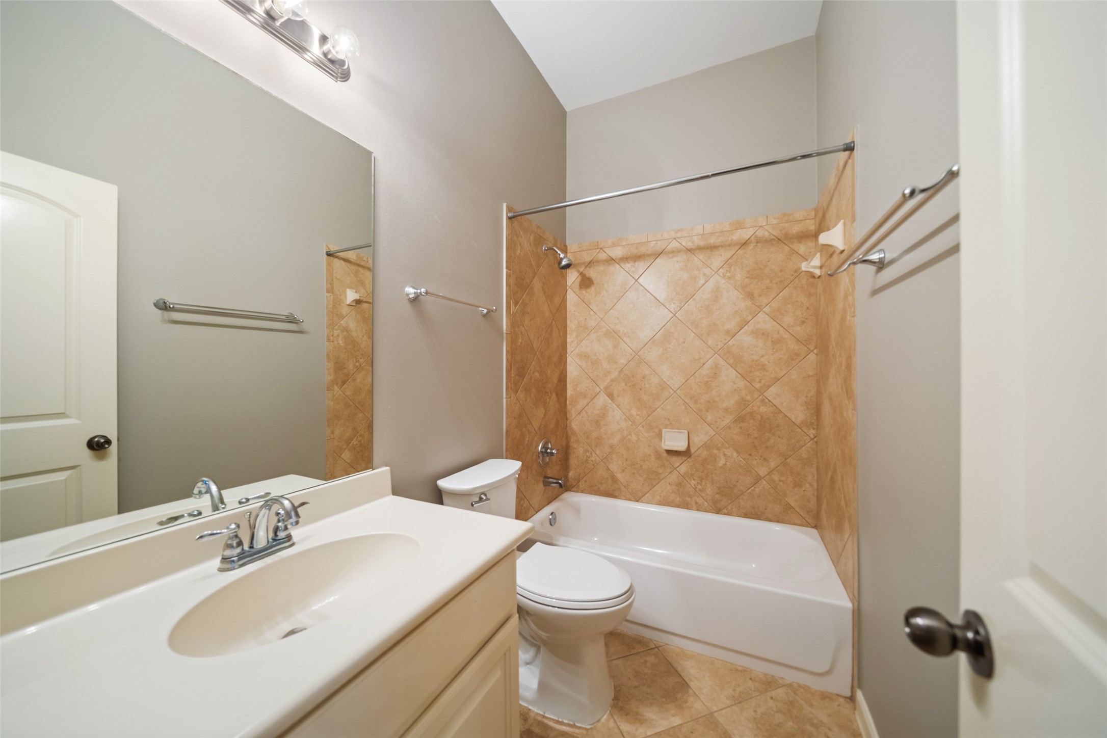 2818 Red Maple Drive Katy, TX 77494 - Photo 23 of 50 En-Suite bathroom features a clean design with a white vanity, modern fixtures, and a large mirror. The bathtub is surrounded by neutral-toned tile, complementing the light-toned walls and floor.