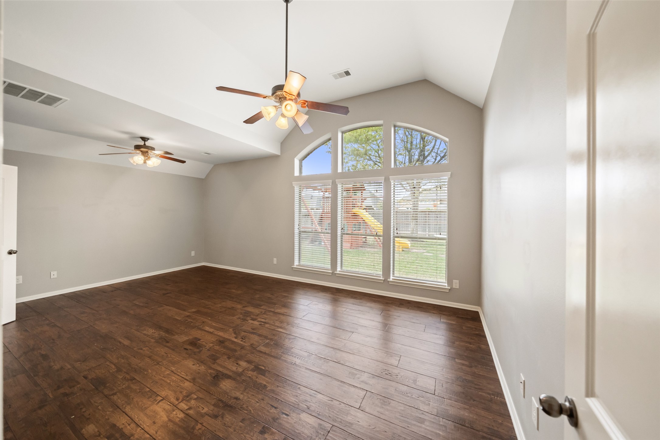 2818 Red Maple Drive Katy, TX 77494 - Photo 34 of 50 Spacious Primary Suite features two ceiling fans and rich wood flooring. Large arched windows offer ample natural light and a view of the backyard, creating a bright and inviting atmosphere.