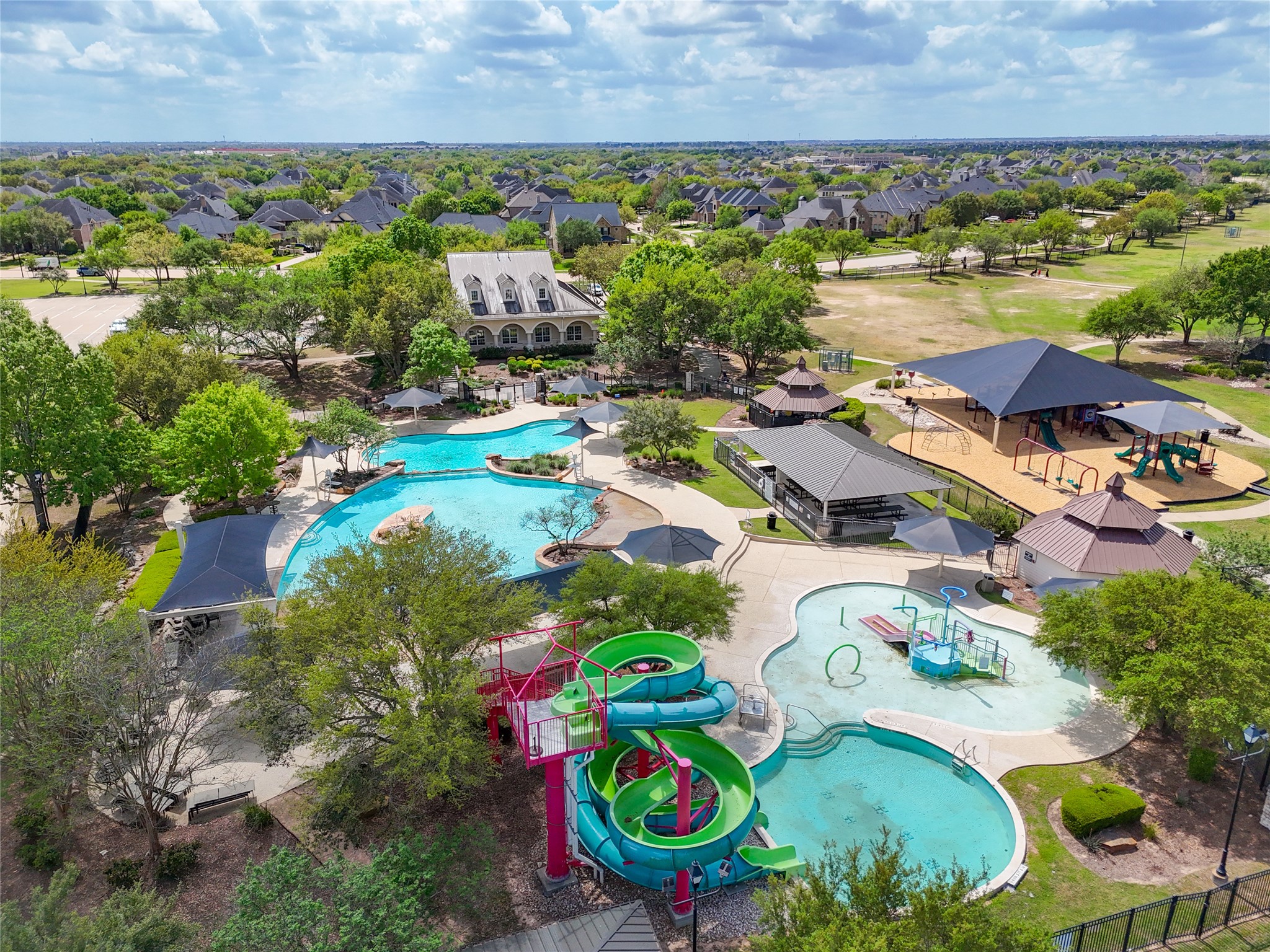 2818 Red Maple Drive Katy, TX 77494 - Photo 46 of 50 Vibrant community park featuring a large swimming pool with water slides, a children's splash area, and a spacious playground. The area is surrounded by lush greenery and offers shaded picnic spots, perfect for family activities. Nearby, a charming clubhouse adds to the community amenities.