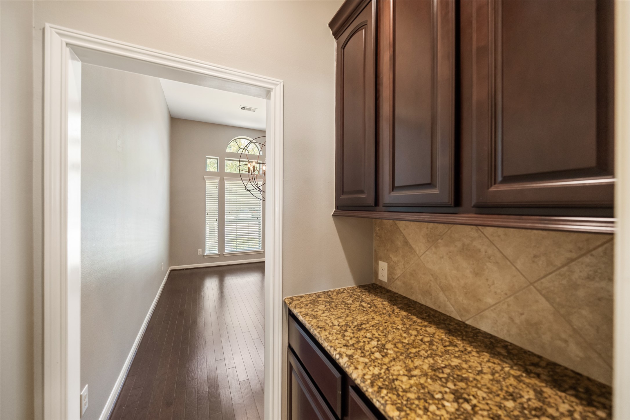 2818 Red Maple Drive Katy, TX 77494 - Photo 9 of 50 This photo showcases a hallway with dark wood flooring and a built-in cabinet featuring granite countertops. The space opens to the large dining room, which features large windows and a modern light fixture, providing ample natural light.
