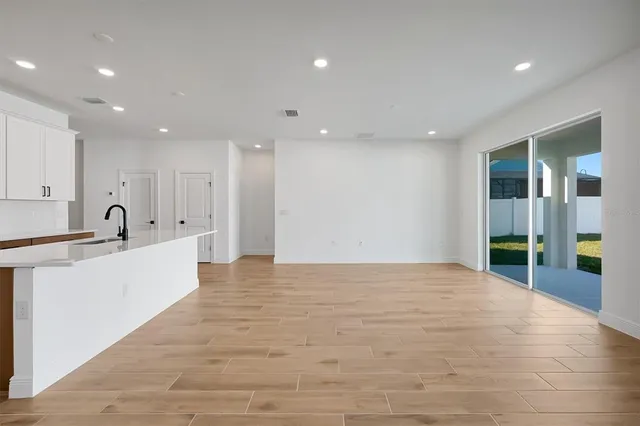 a view of an empty room with kitchen and window