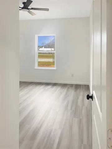 an empty room with wooden floor ceiling fan and windows