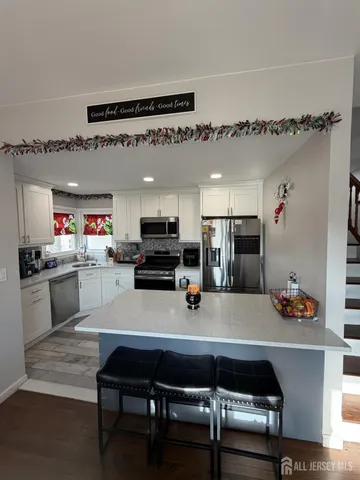 a living room with stainless steel appliances furniture a rug and a kitchen view