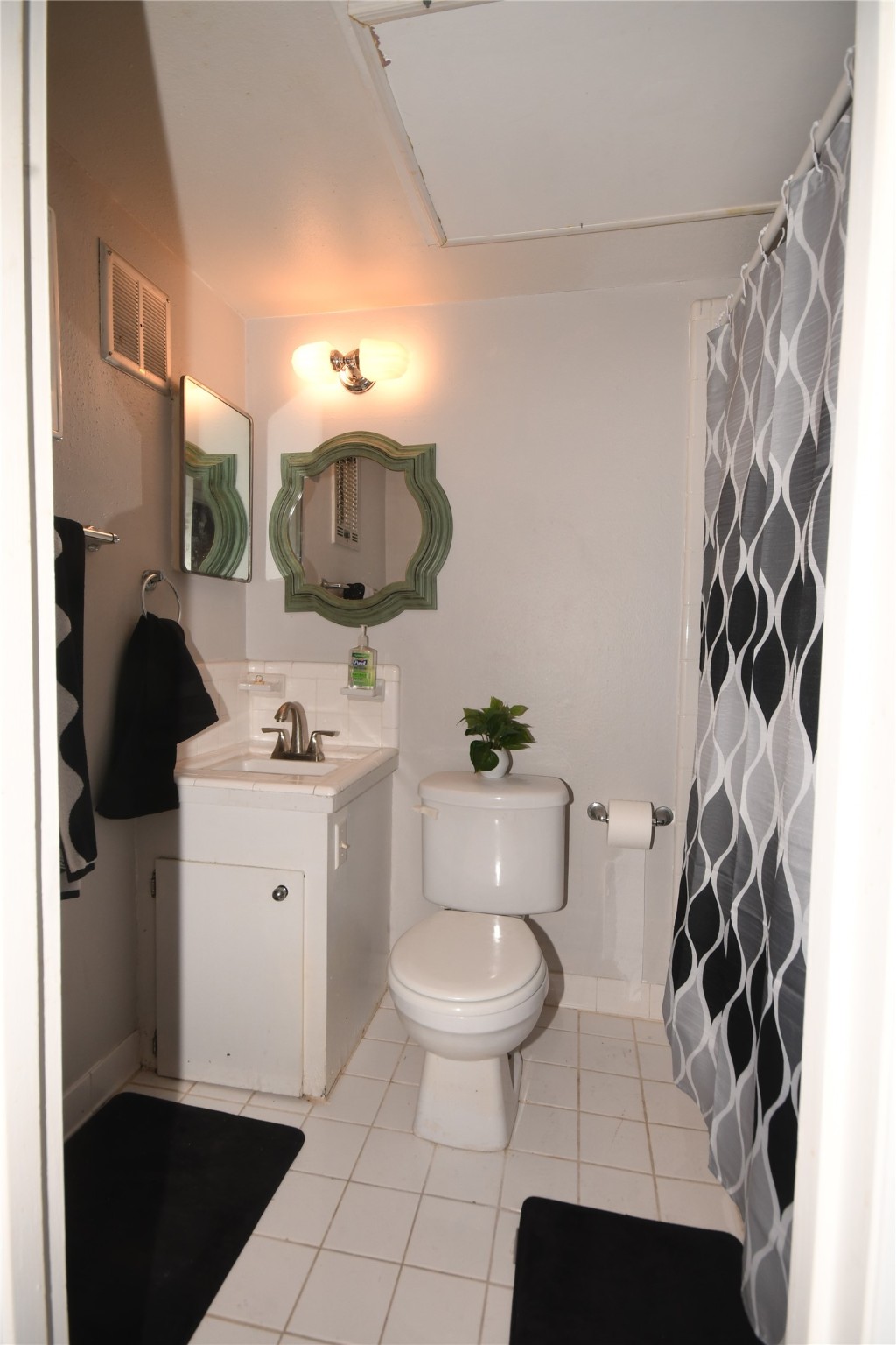 3401 Timmons Lane, Unit 12 Houston, TX 77027 - Photo 6 of 9 This is a compact bathroom has a shower tub with a patterned curtain and is accented with black accessories. The space has a clean, minimalist design.