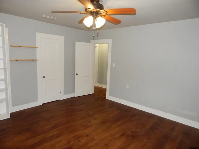 an empty room with wooden floor fan and windows
