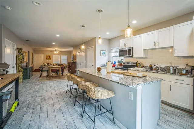 a kitchen with stainless steel appliances granite countertop a refrigerator a stove top oven a sink dishwasher and white cabinets with wooden floor