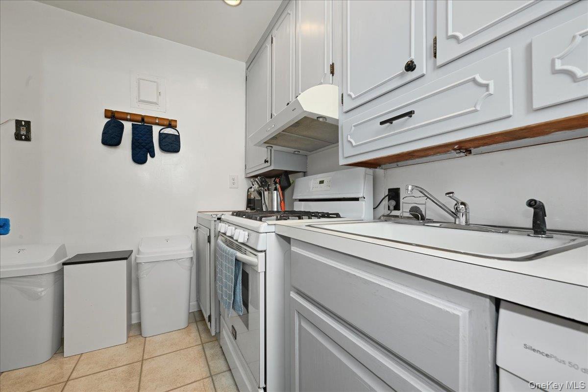 218-03 68th Avenue, Unit 1 Queens, NY 11364 - Photo 8 of 13 Kitchen featuring white gas range oven, light countertops, under cabinet range hood, light tile patterned floors, and gray cabinets