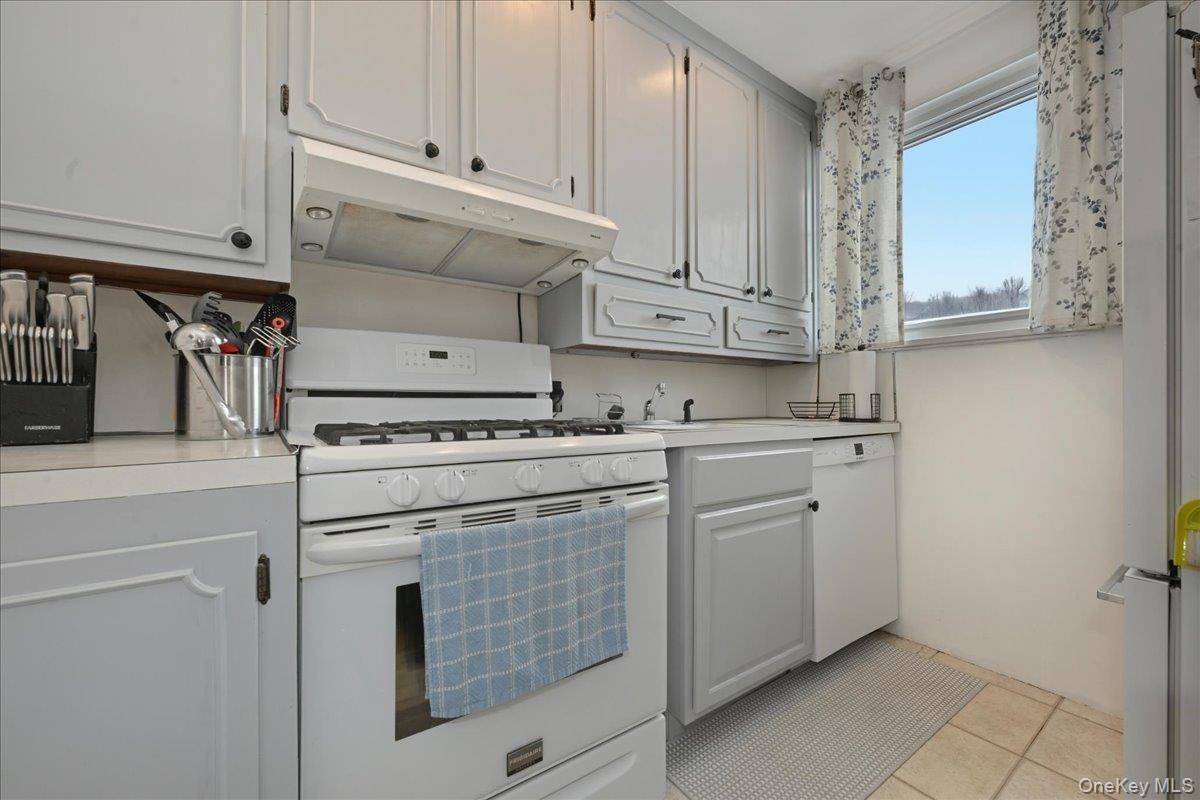 218-03 68th Avenue, Unit 1 Queens, NY 11364 - Photo 9 of 13 Kitchen with white appliances, under cabinet range hood, light countertops, white cabinets, and light tile patterned floors