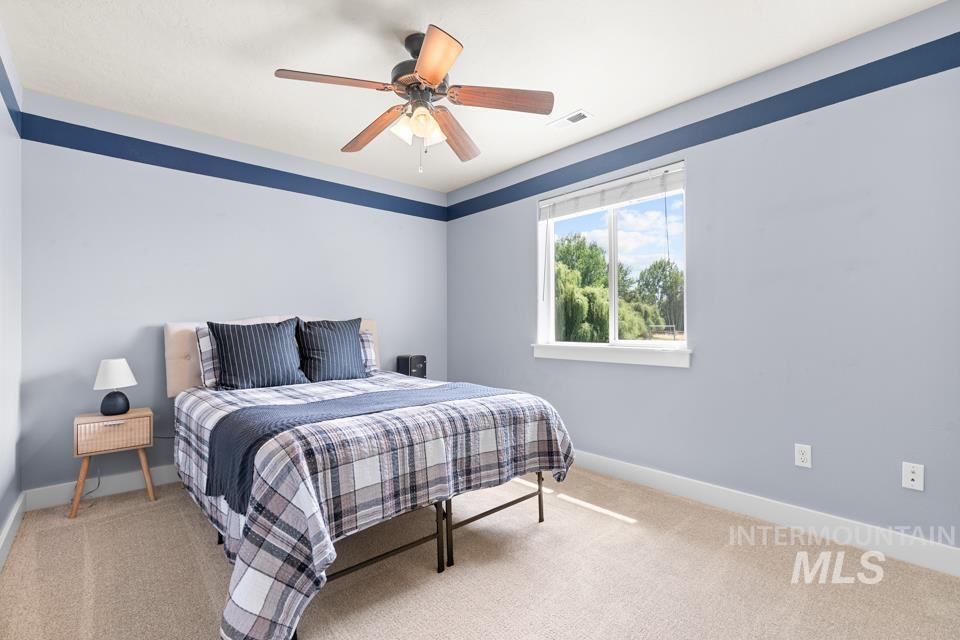 23800 Breyer Road Caldwell, ID 83607 - Photo 29 of 50 Carpeted room featuring a ceiling fan, a window with exterior tree scenery, and light-colored walls with a contrasting accent stripe