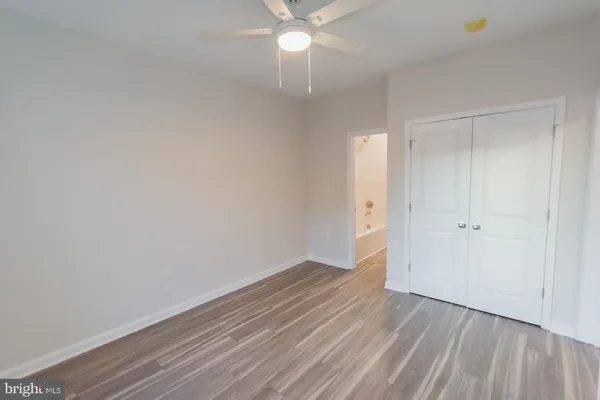 a view of an empty room with wooden floor and a ceiling fan