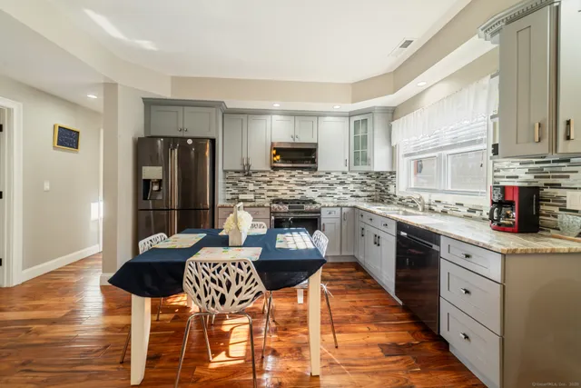 a kitchen with stainless steel appliances kitchen island granite countertop a refrigerator a stove a sink dishwasher and a dining table with wooden floor