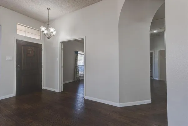 an empty room with wooden floor chandelier and windows