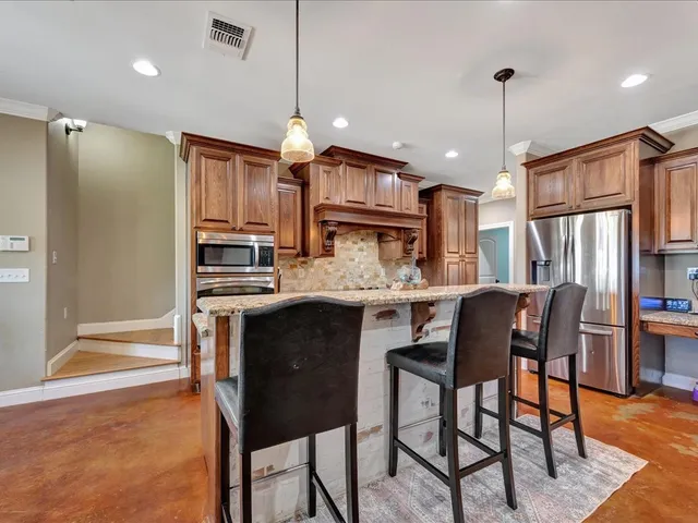 a kitchen with stainless steel appliances granite countertop a refrigerator a stove a sink dishwasher and a dining table with wooden floor