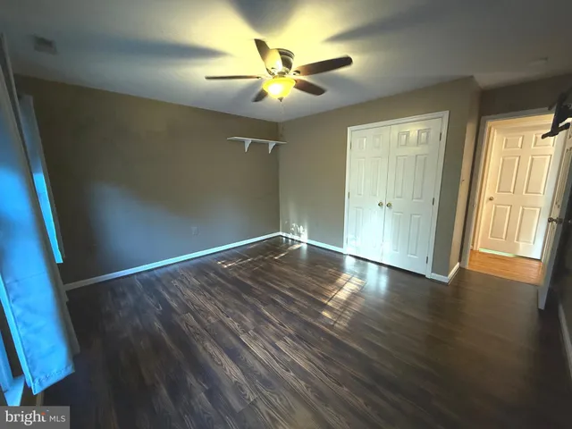 a view of an empty room with wooden floor and a ceiling fan