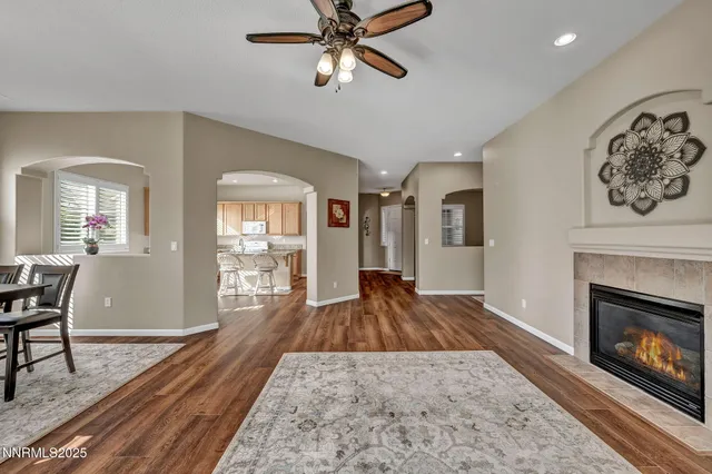 a view of a livingroom with a fireplace a ceiling fan and wooden floor